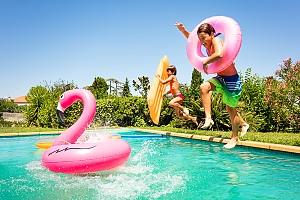 Kids with flamingo floats jumping into swimming pool
